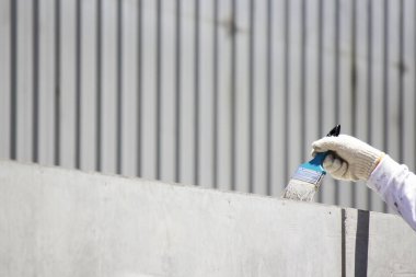 Eldiven giyen kişi bir yüzeyi fırçayla boyar ya da kaplar.