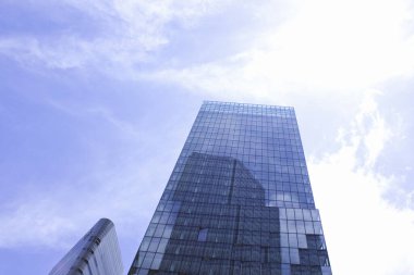 Modern cam gökdelen mavi gökyüzüne karşı güneş ışığını yansıtıyor