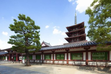 Japon pagodası mavi gökyüzünün altındaki yeşil ağacın yanında duruyor.