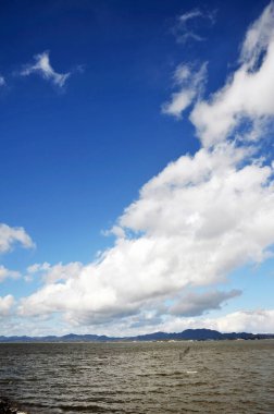 Uzak dağların üzerindeki mavi gökyüzü ve sakin su yüzeyi