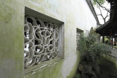 Süslü taş kafes pencereleri eski yosunlu bahçe duvarını dekore ediyor.