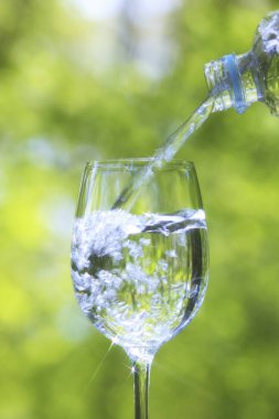 Bulanık yeşil arka planda suyu şarap bardağına dökmek