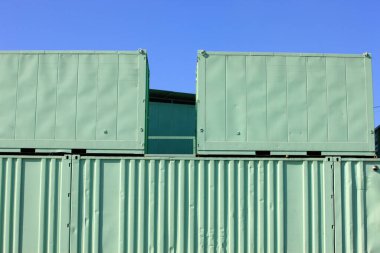 Temiz gökyüzünün altında yığılmış yeşil nakliye konteynerleri