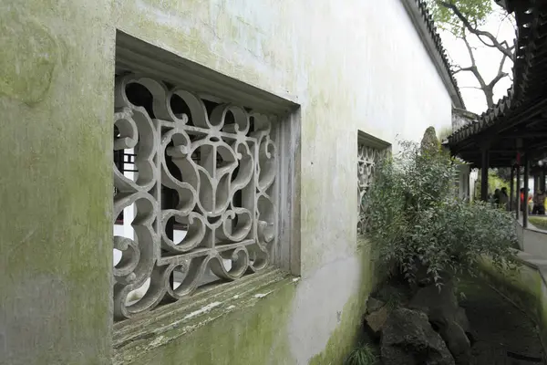 Süslü taş kafes pencereleri eski yosunlu bahçe duvarını dekore ediyor.