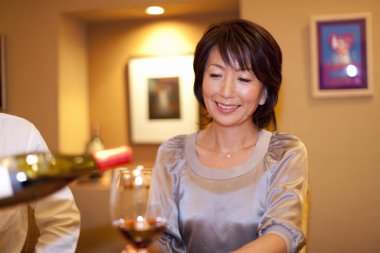 Asyalı olgun bir kadın ve şişeden kırmızı şarap dökülüyor.