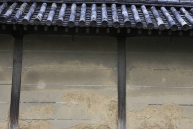 Yıpranmış kil duvar, koyu kiremitli çatı yapısını destekliyor.