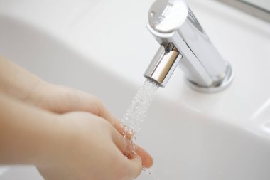 Kadın ellerini banyoda suyun altında yıkıyor.