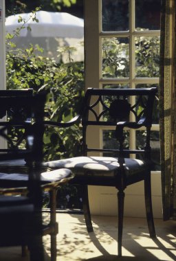 Pencereden süzülen güneş ışığı boş ahşap sandalyeleri aydınlatıyor