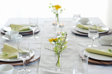Akşam yemeği için beyaz tabaklar, şarap bardakları, yeşil peçeteler ve sarı çiçekler. 