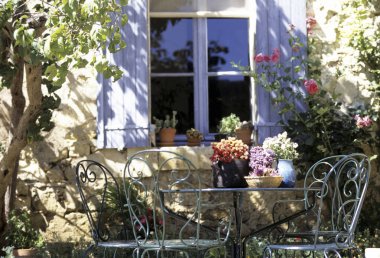 Güzel bir teras, saksı bitkileri ve güneşli bir günde sandalyeli bir masa.