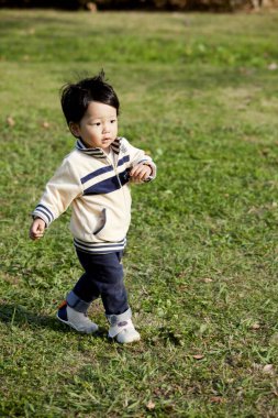 Parktaki çimlerde oynayan yakışıklı Asyalı çocuk. 