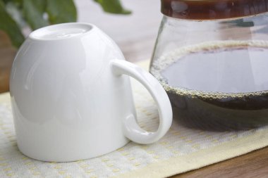 Beyaz seramik kahve fincanı cam kahve demliğinin yanında dinleniyor.