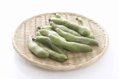 Beyaz arkaplanda bambu sepetinin üzerindeki taze bezelye kabuklarının yakın plan görüntüsü