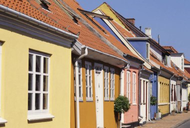 Açık mavi gökyüzünün altında sessiz cadde boyunca uzanan renkli evler