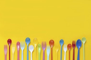 Sarı arka planda renkli plastik çatal bıçak seti. en üstteki görünüm     