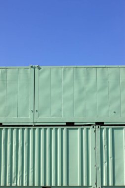 Açık mavi gökyüzü arkaplanına karşı yeşil metal nakliye konteynırı