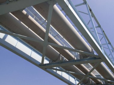 Büyük endüstriyel borular mavi çelik köprüyü geçiyor.