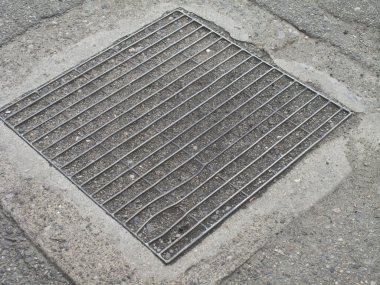 Kaldırımdaki kanalizasyon deliğini kaplayan metal ızgara.