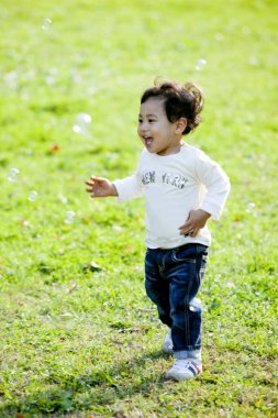 Parktaki çimlerde oynayan yakışıklı Asyalı çocuk. 