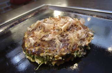 Lezzetli bir Japon gözlemesi olan Okonomiyaki, buğday unu hamuru ve lahana, et ve deniz ürünleri gibi çeşitli malzemelerle yapılan ve bir teppan üzerinde pişirilen 