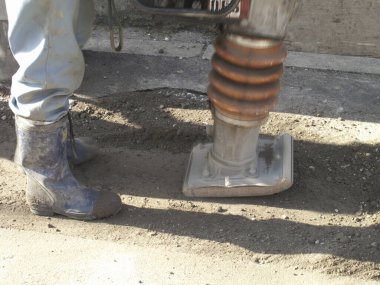 İnşaat alanındaki toprağı sıkıştırmak için makine kullanan işçiler
