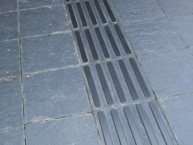 Doğrusal drenaj ızgaraları içeren gri taş asfalt yüzey boyunca