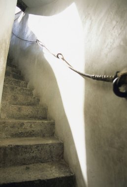 Güneş ışığı, metal tırabzanlarla dar taş merdivenleri aydınlatıyor.