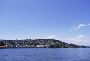 Sakin mavi göl küçük tepe kenarı kasaba binalarının yakınlarında gökyüzünü yansıtıyor.