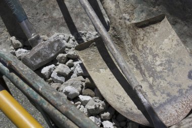 Paslı kürekler ve balyoz dağınık beton molozların arasında duruyor.