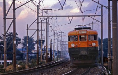 Turuncu elektrikli tren gün batımında tren rayları boyunca ilerliyor.