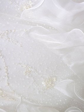 Zarif beyaz kumaş, pırıl pırıl pullar ve nakışla süslenmiş.