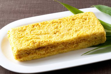 Beyaz tabakta yeşil yapraklı sarı Japon omleti.