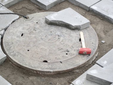 İnşaat sırasında etrafı kaldırım taşlarıyla çevrili beton rögar kapağı.