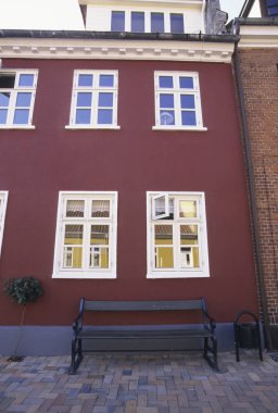 Beyaz pencereli kırmızı tuğla bina ve dışarıda boş bank