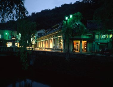 Aydınlatılmış geleneksel bina, alacakaranlıkta sakin suyun yanında yansıyor.