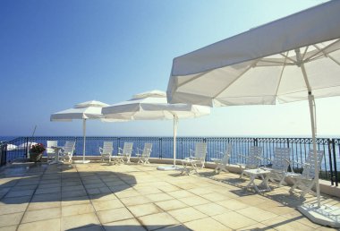 Terastaki beyaz şemsiyeli ve sandalyeli güzel deniz manzarası.       