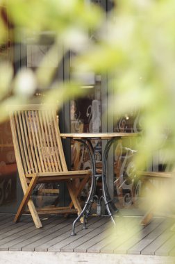 Ahşap masa ve caddede sandalyeler, ön planda bulanık ağaç