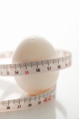 Beyaz arka planda beyaz bir yumurtanın ölçüm bandıyla yakın plan çekimi.