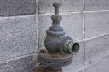 Beton blok duvarına bağlı paslı endüstriyel valf.