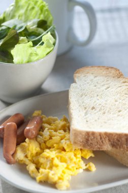 Kahvaltıda yumurta, ekmek, sosis ve salata. 