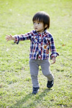 Parktaki çimlerde oynayan yakışıklı Asyalı çocuk. 