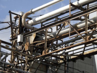 Paslı endüstriyel borular gökyüzüne karşı metal iskeleti kesiştiriyor