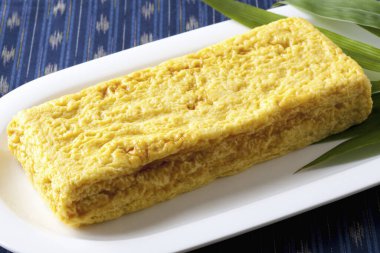 Beyaz tabakta yeşil yapraklı sarı Japon omleti.