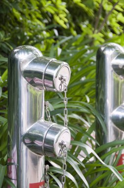 Yeşil yapraklar ve bitkilerle çevrili metal yangın muslukları.