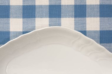 Arkaplanda kareli peçete olan beyaz tabak