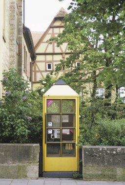 Kereste kaplı evin yanındaki yeşil çalıların arasında duran sarı telefon kulübesi.