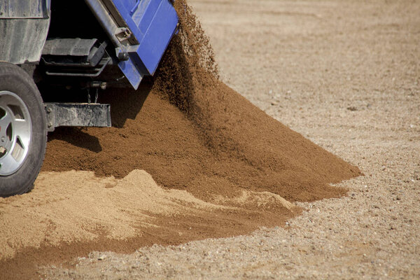 Dump truck unloading brown sand onto dry ground surface