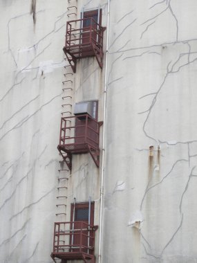 Üç paslı yangın çıkışından oluşan yıpranmış bina duvarı.