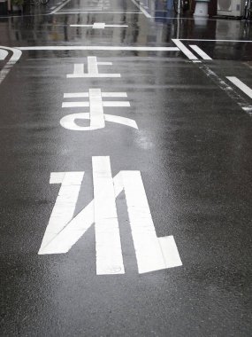 Islak sokak, kaldırımda beyaz boyalı trafik işaretleri gösteriyor.