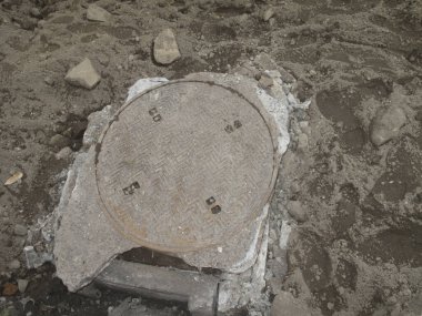 Yıpranmış beton rögar kapağı sert topraklarla çevrili.